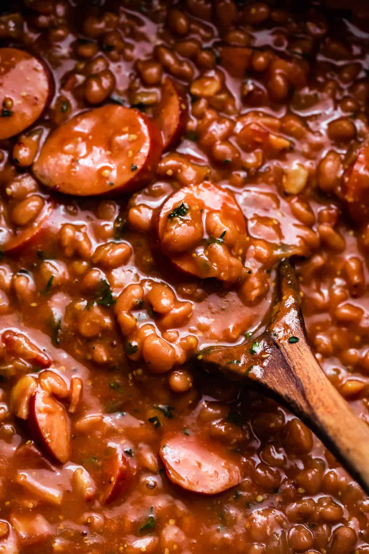 wooden spoon stirring through baked beans and sausage.