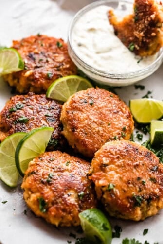 five air fryer fish cakes set on a platter with a garnish of lime slices and a dipping sauce set on the side.