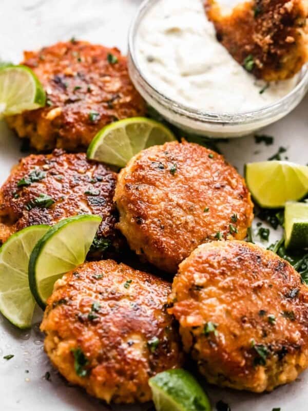five air fryer fish cakes set on a platter with a garnish of lime slices and a dipping sauce set on the side.