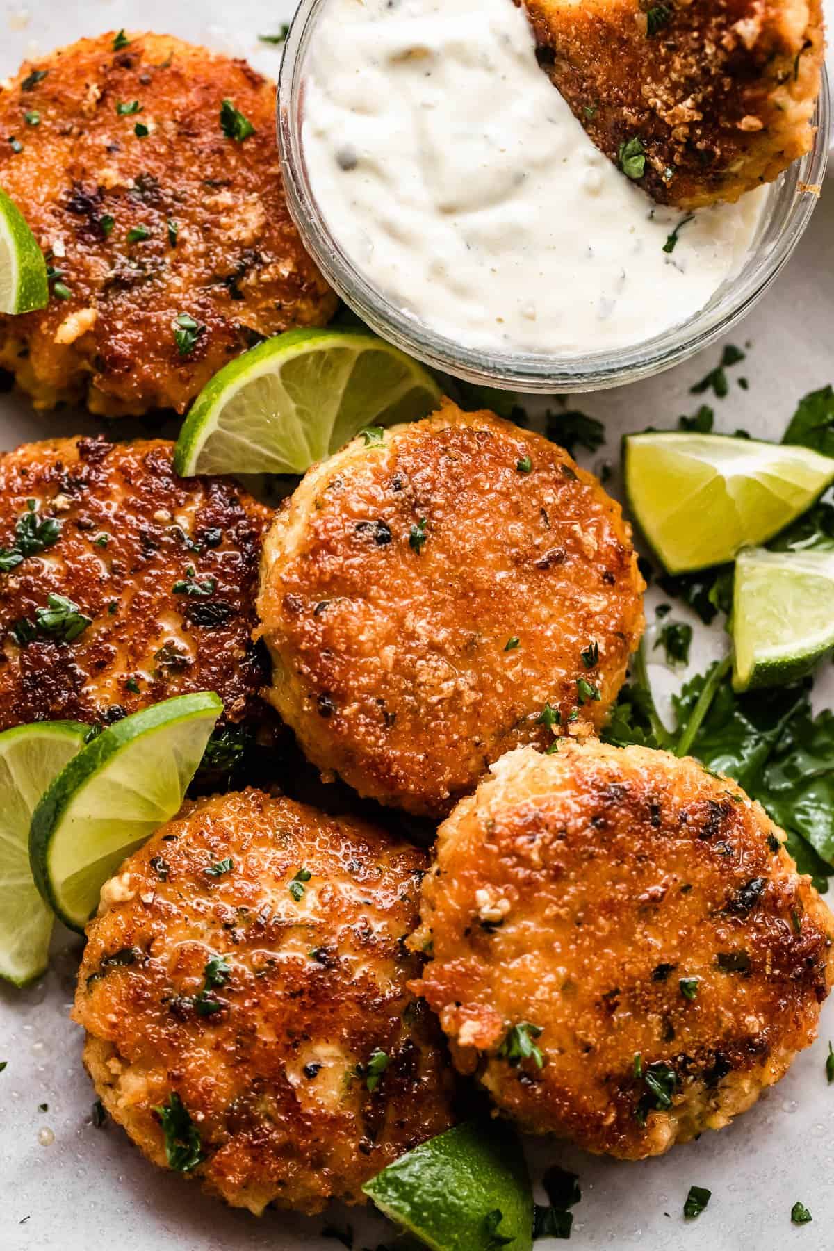 five fish cakes set on a platter with a garnish of lime slices and a dipping sauce set on the side.