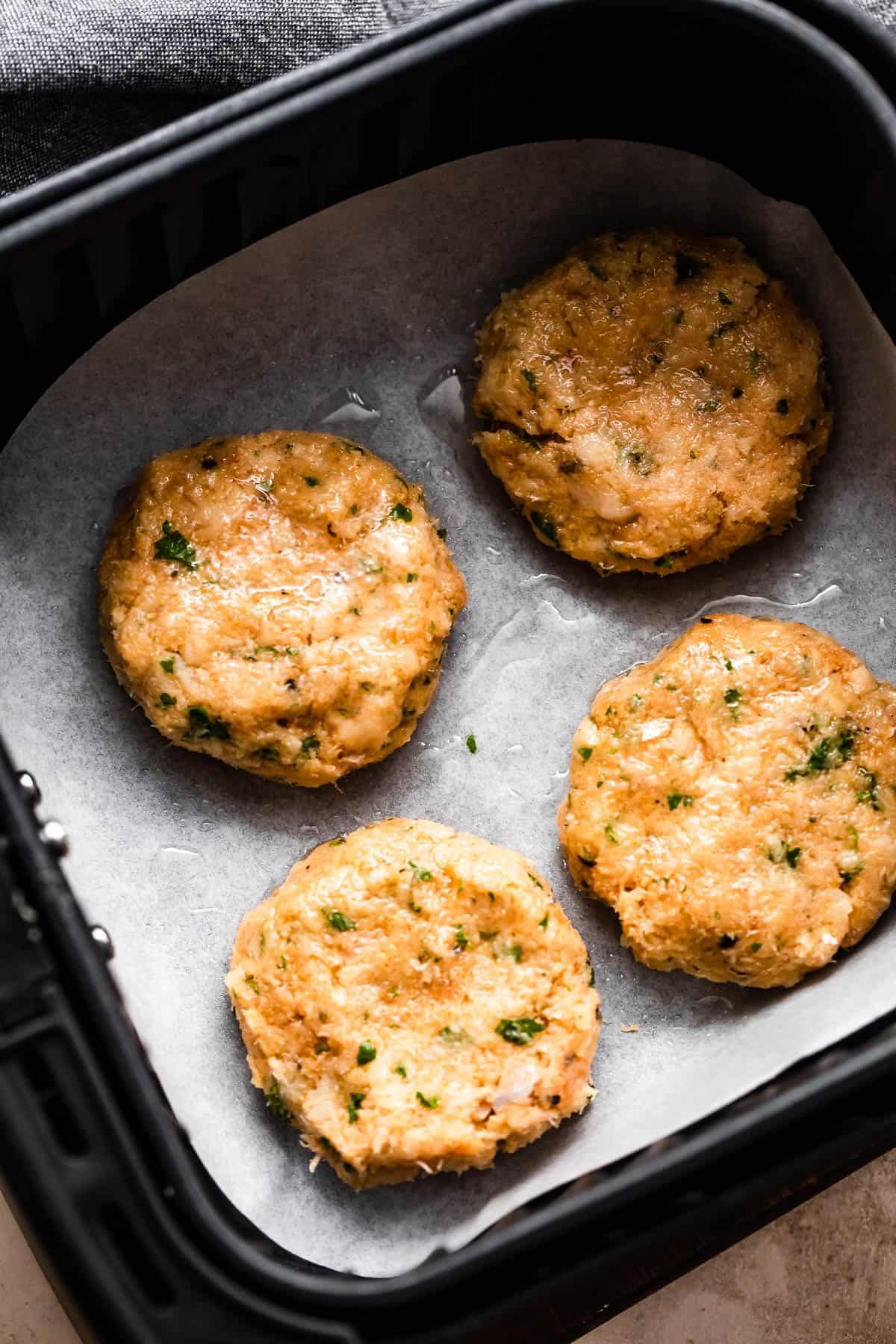 four raw fish cakes in an air fryer basket