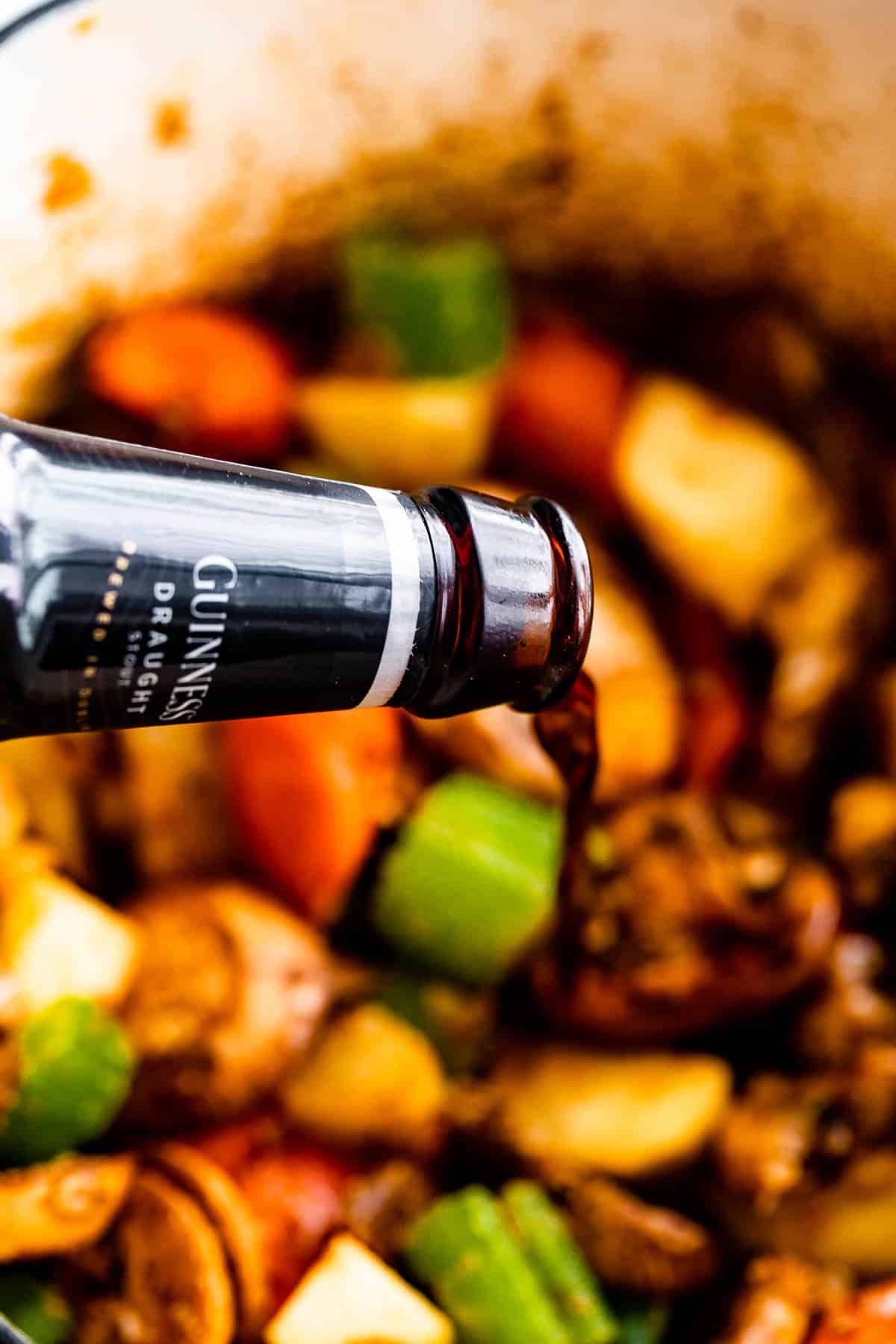 pouring guinness beer over chopped vegetables and beef chunks inside a pot.