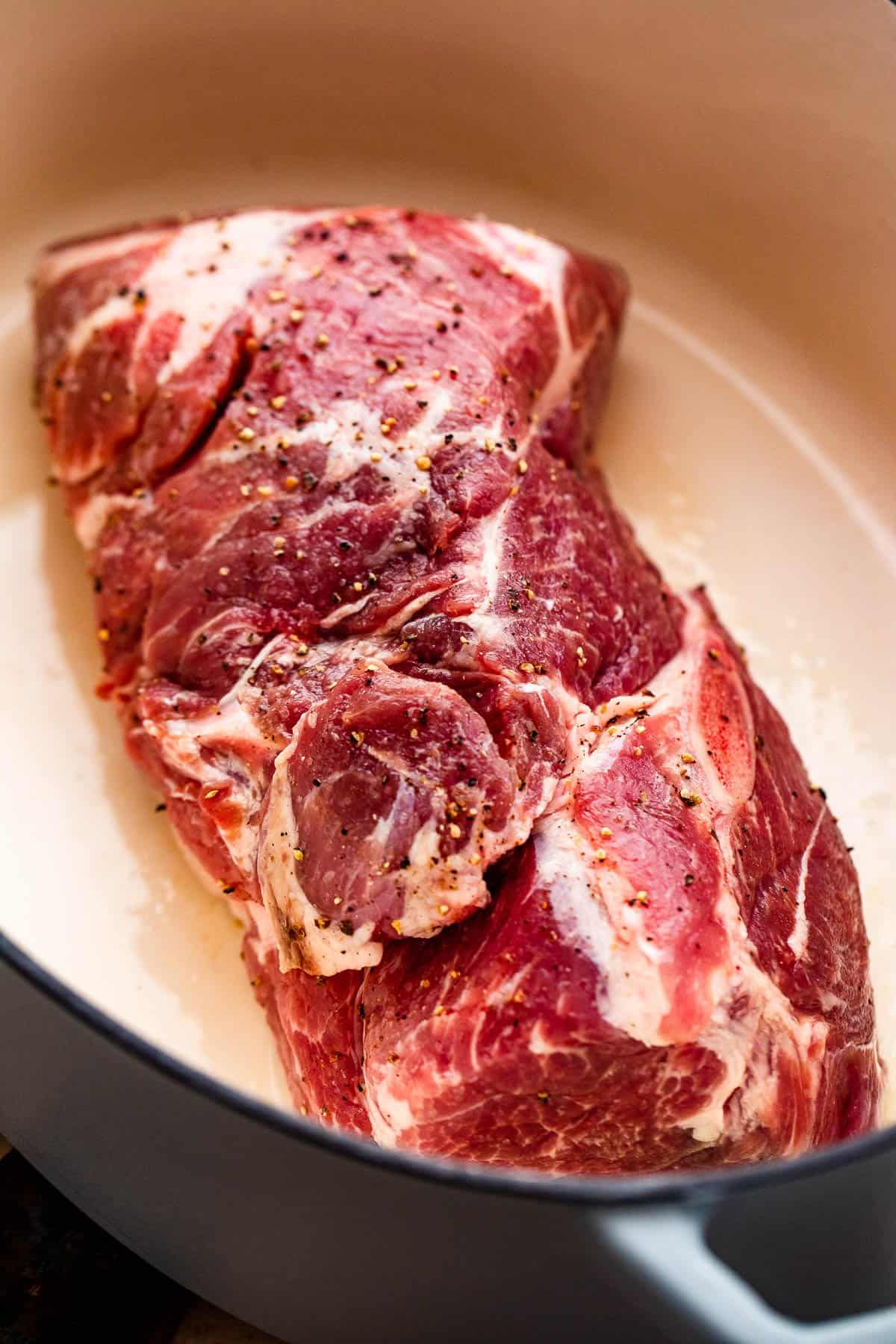 Seasoned raw pork shoulder browning in a Dutch oven.