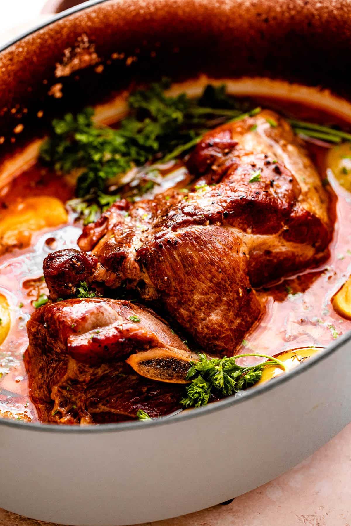 Close-up photo of a Dutch oven with pork shoulder sitting in a sauce with apple slices and greens.