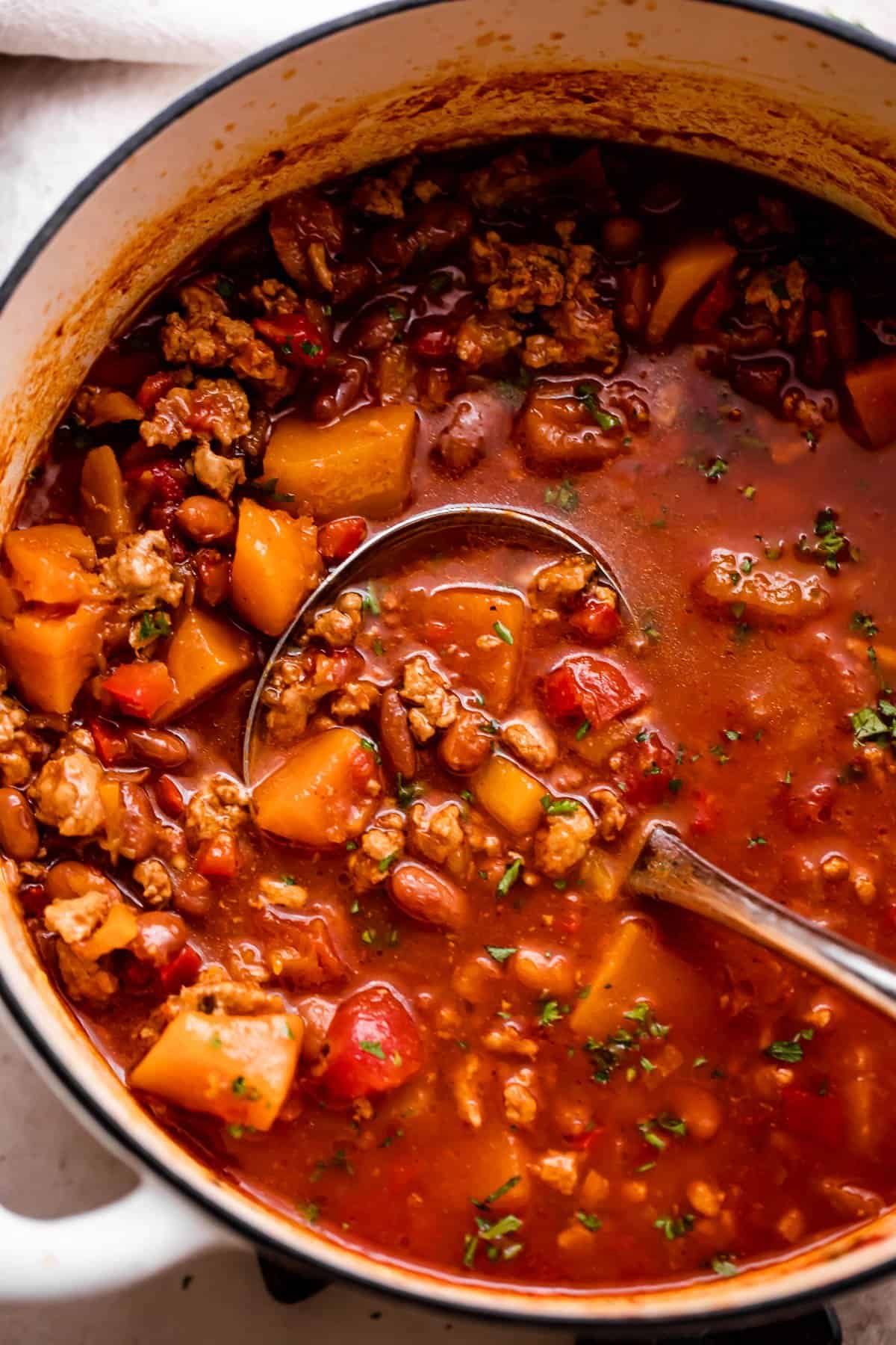 Overhead shot of a soup pot with cooked turkey chili with butternut squash in a tomato-based broth.