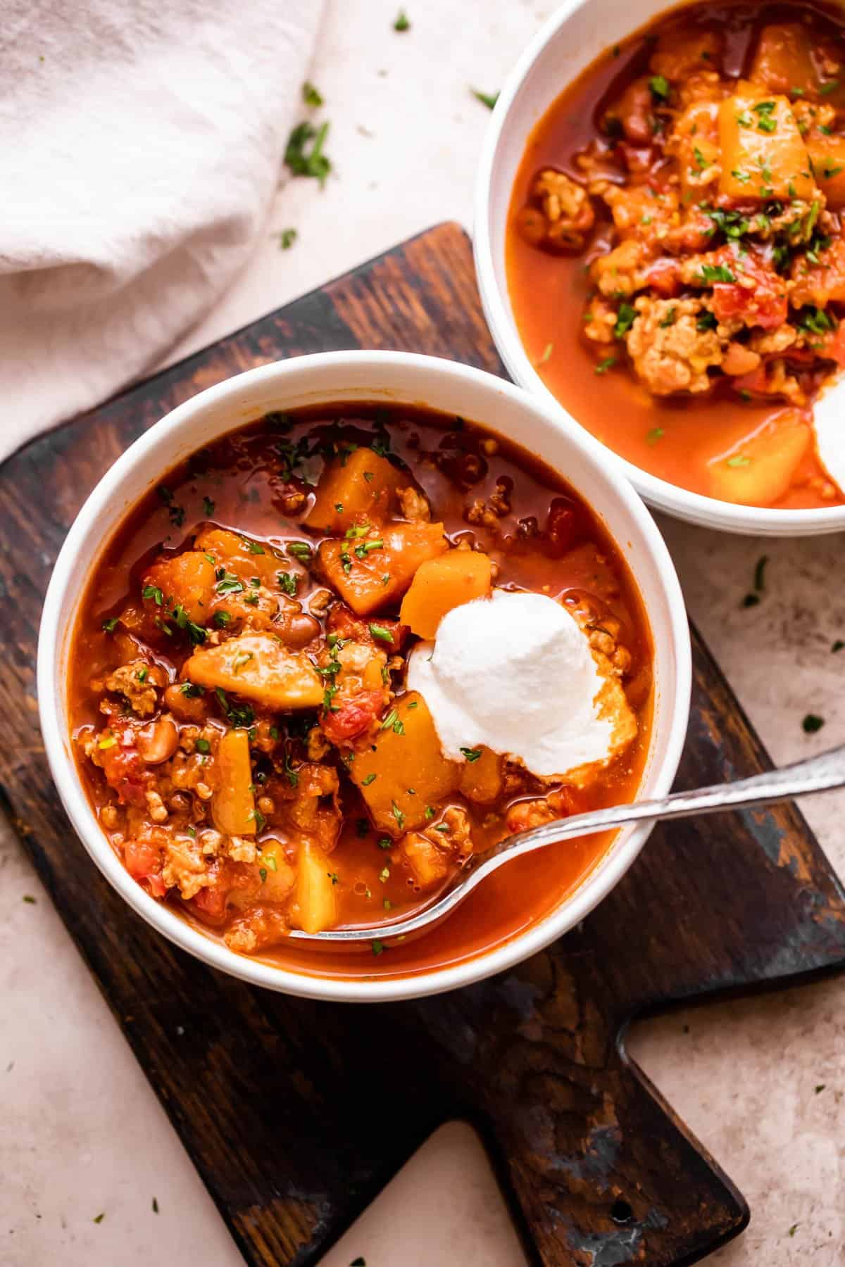 Overhead shot of two white soup bowls filled with turkey chili and garnished with a dollop of sour cream.