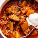 close up shot of a bowl with turkey chili, studded with cubed butternut squash, tomatoes, and a garnish of sour cream.