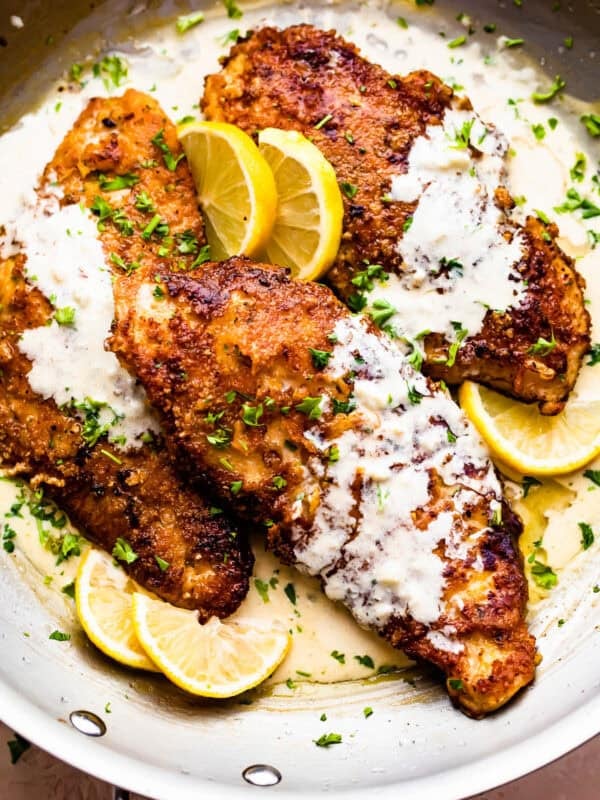 Three turkey cutlets in a skillet topped with cream sauce.