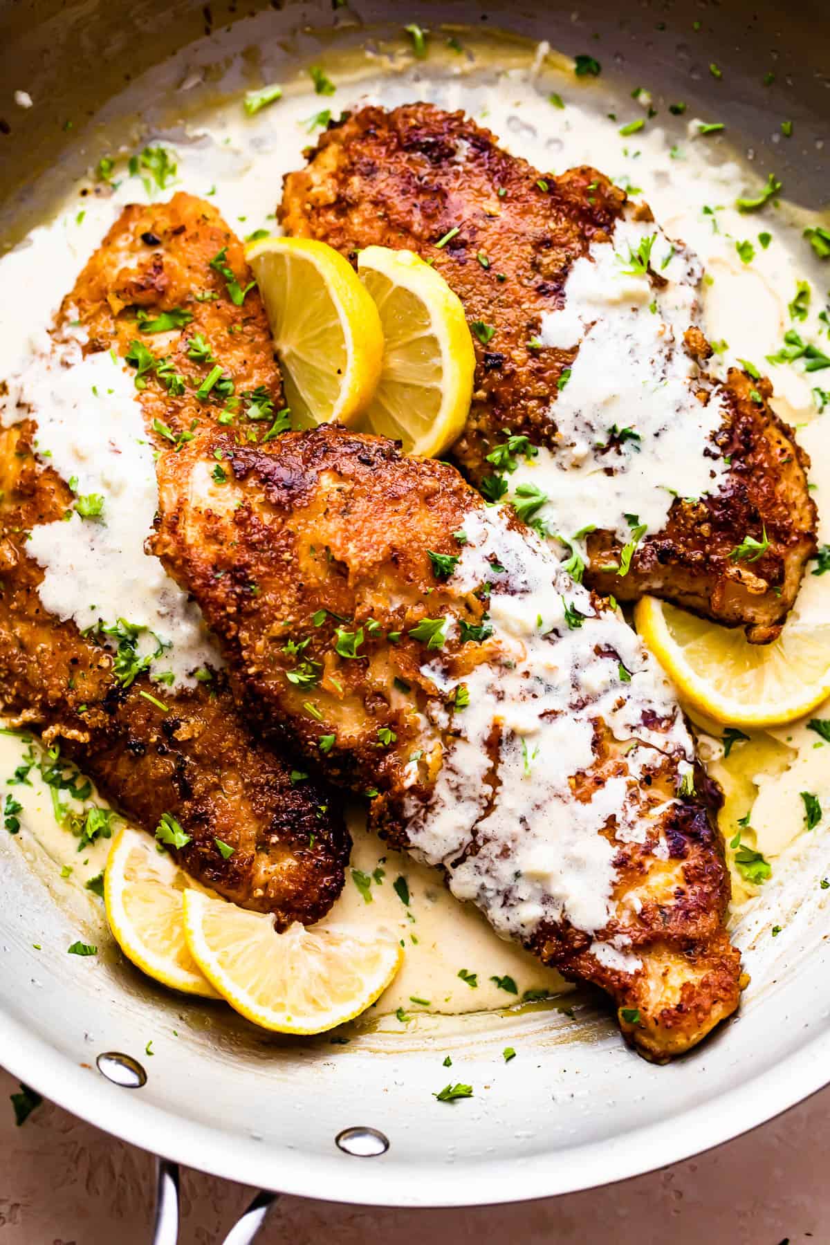 Three turkey cutlets in a skillet topped with cream sauce.