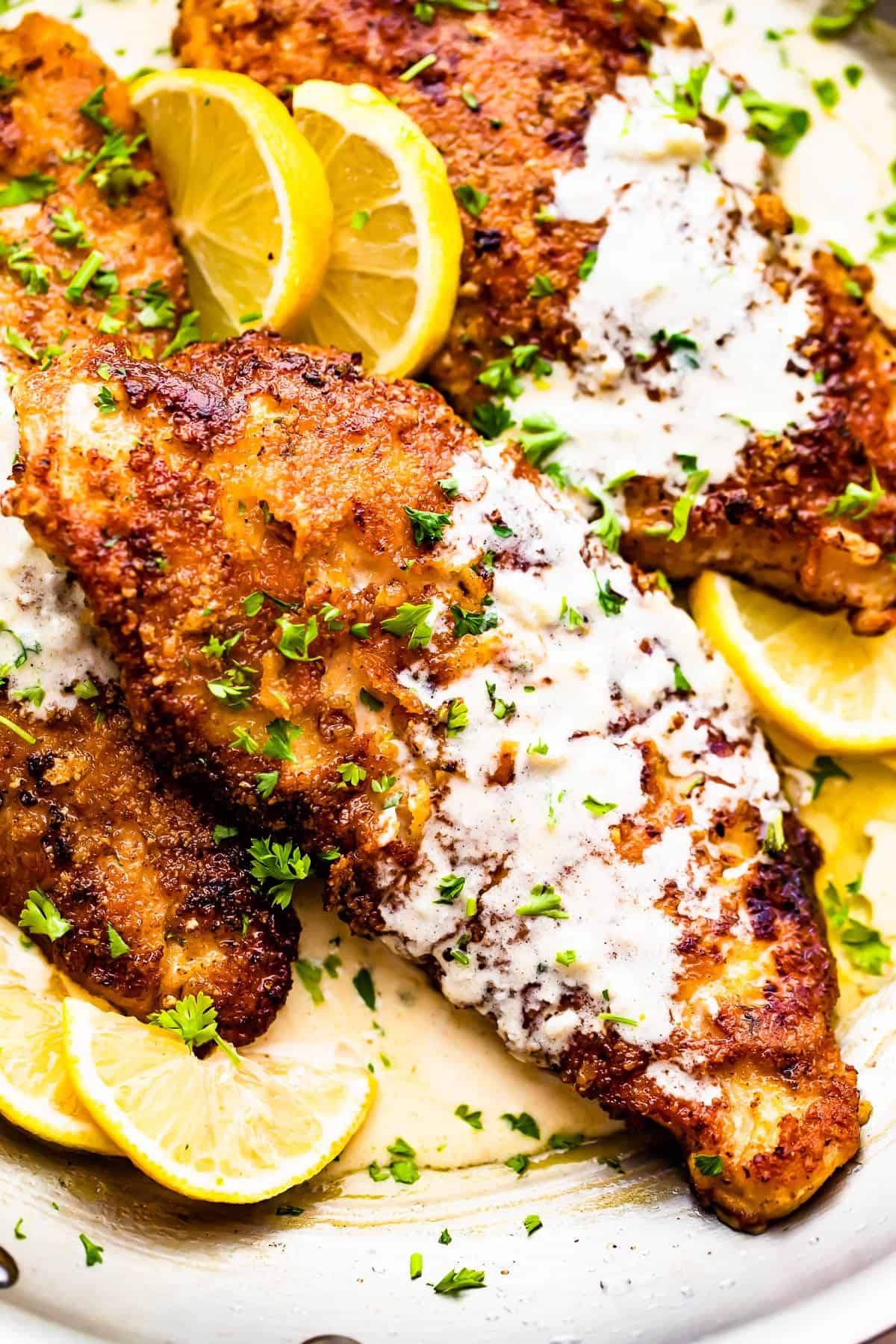 three breaded turkey cutlets topped with creamy lemon sauce and garnished with lemon slices and parsley