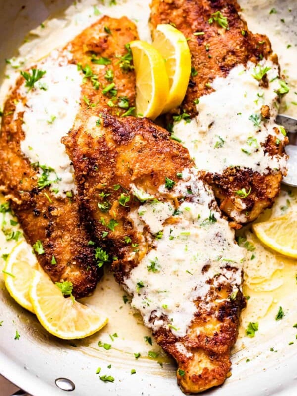 three breaded turkey cutlets topped with creamy lemon sauce and garnished with lemon slices and parsley