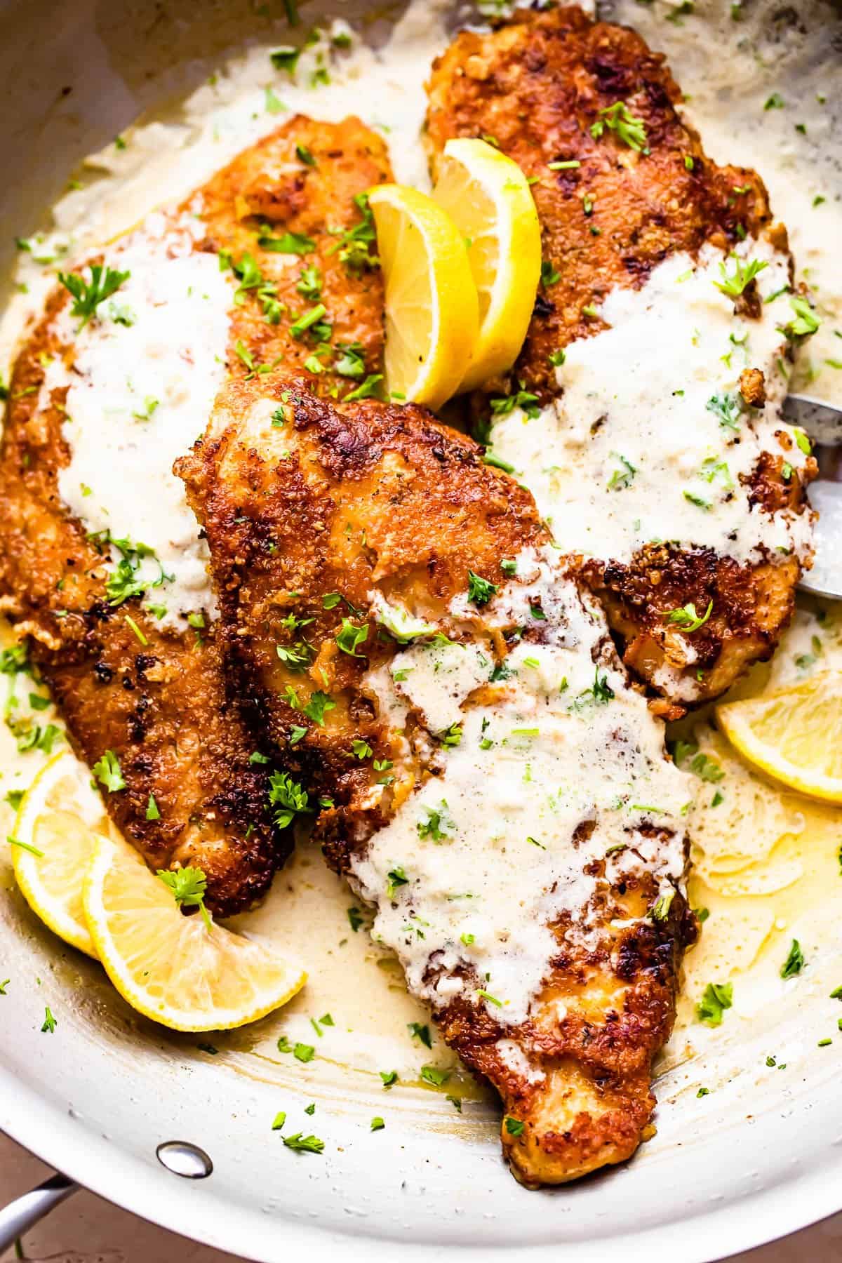 three breaded turkey cutlets topped with creamy lemon sauce and garnished with lemon slices and parsley