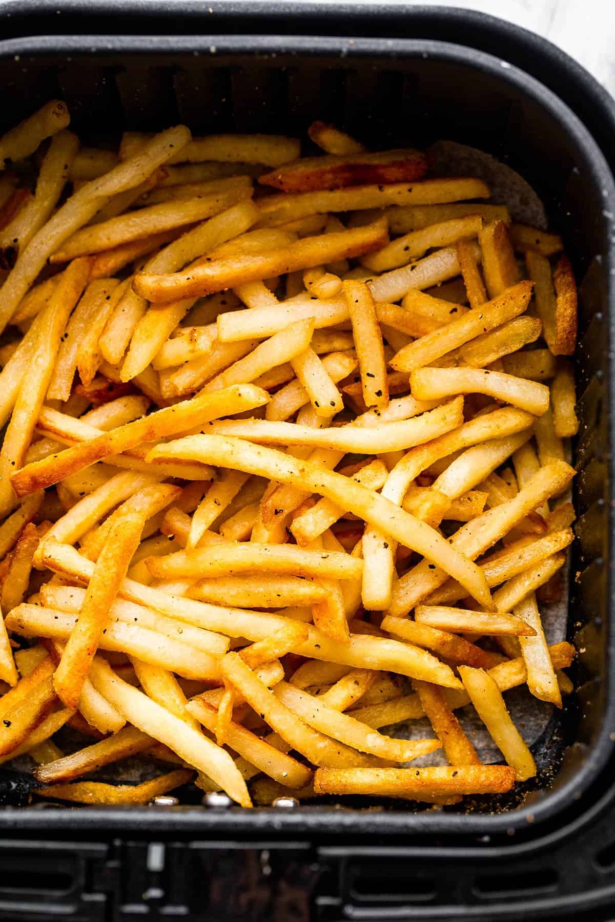 frozen french fries in a black air fryer basket.