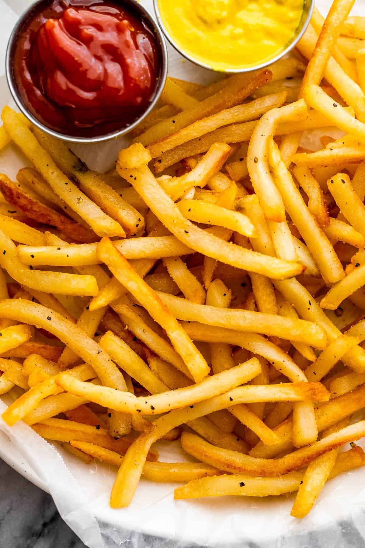 overhead shot of a plate with Crispy Air Fryer Frozen French Fries. Little bowls of mustard and ketchup on a plate.