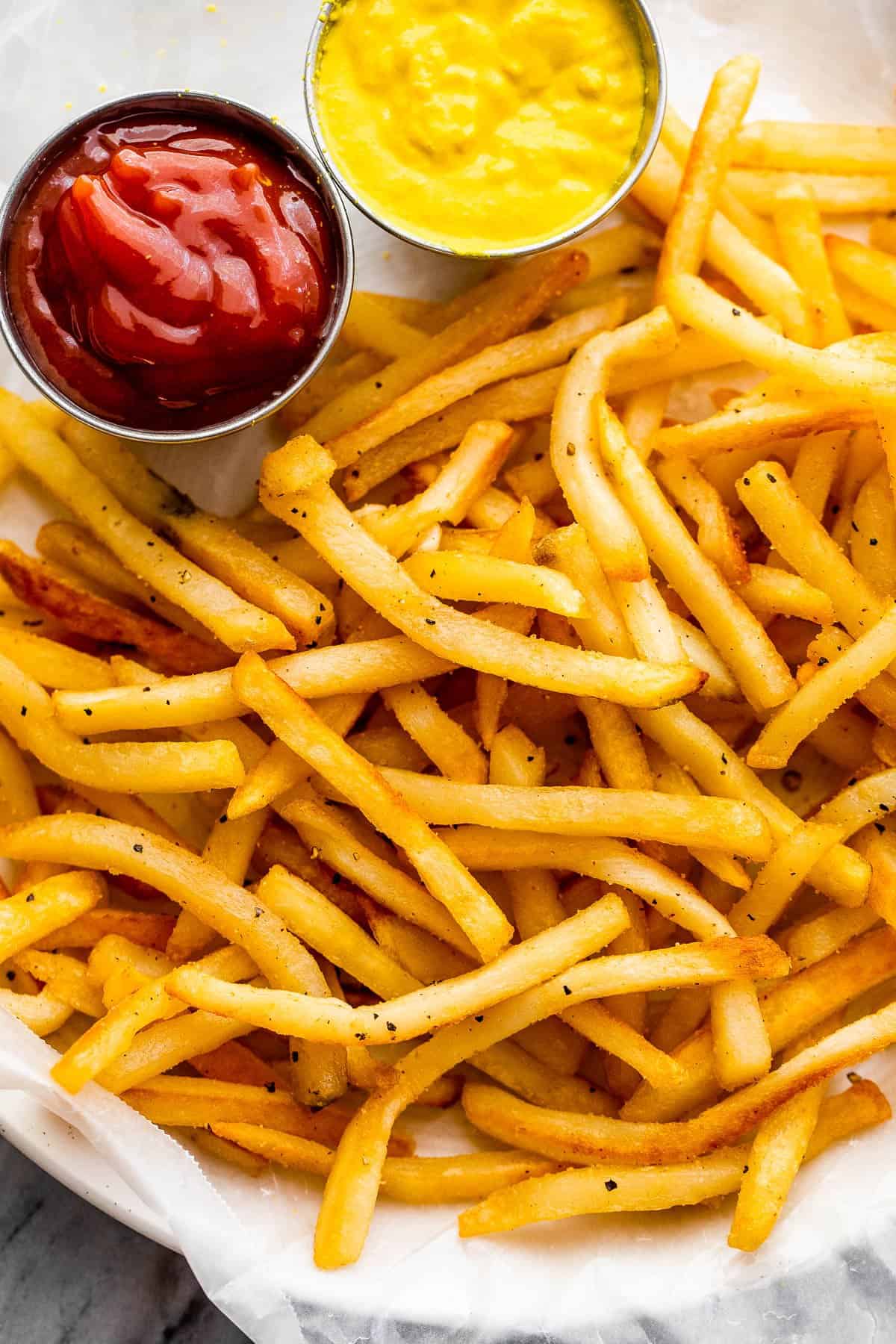 overhead shot of a plate with Crispy Air Fryer Frozen French Fries. Little bowls of mustard and ketchup on a plate.