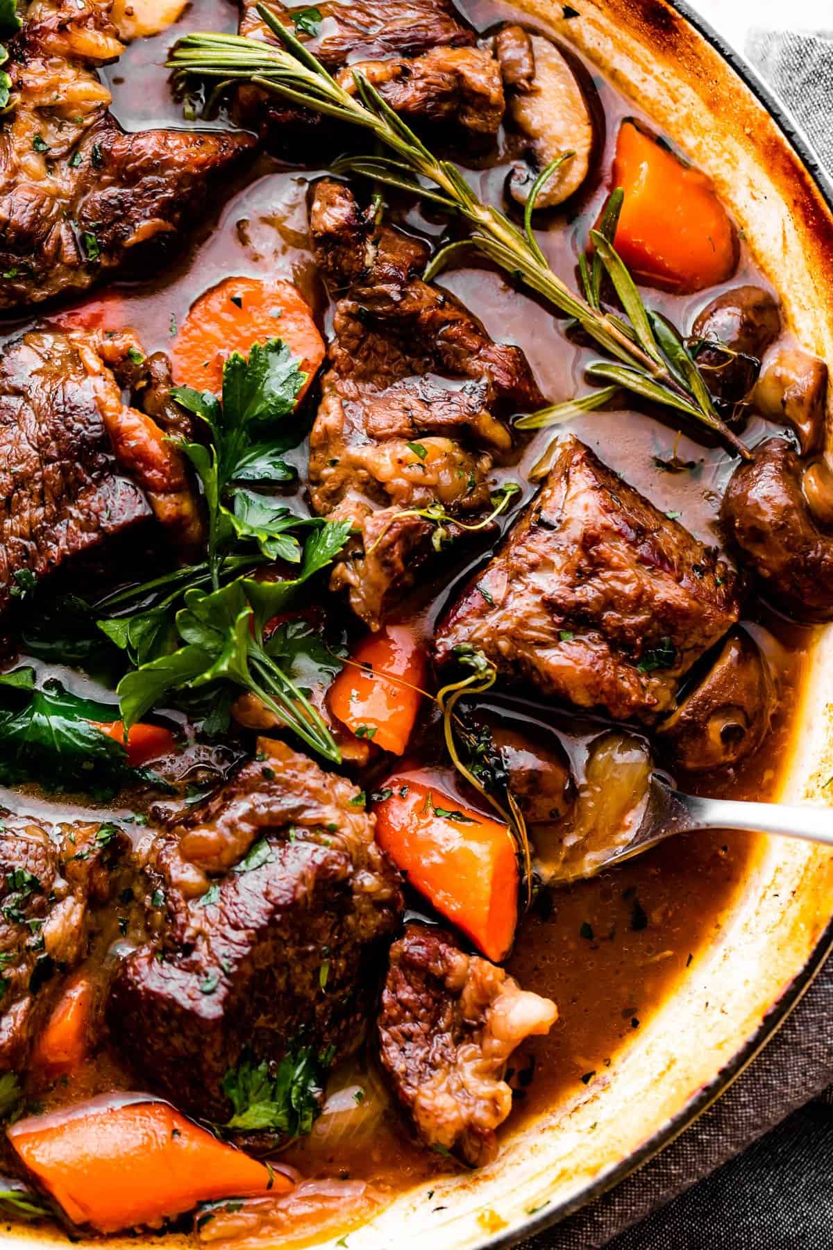Close-up image of cooked pot roast in liquid with carrots and mushrooms.