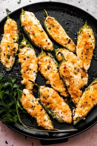 Air Fryer Jalapeno Poppers arranged on a round black plate and garnished with parsley.