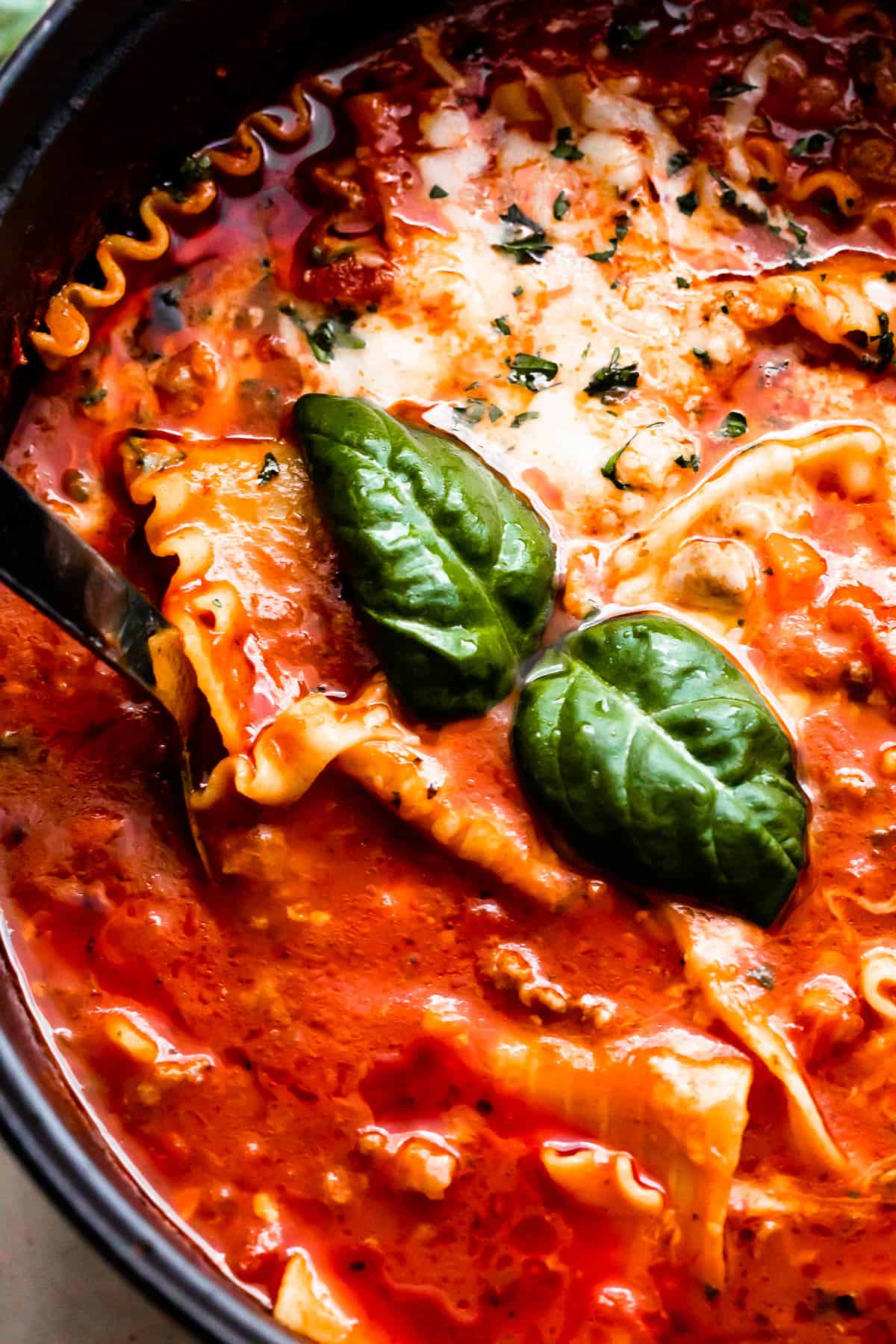 dark dutch oven filled with lasagna soup, garnished with melted cheese and two large basil leaves