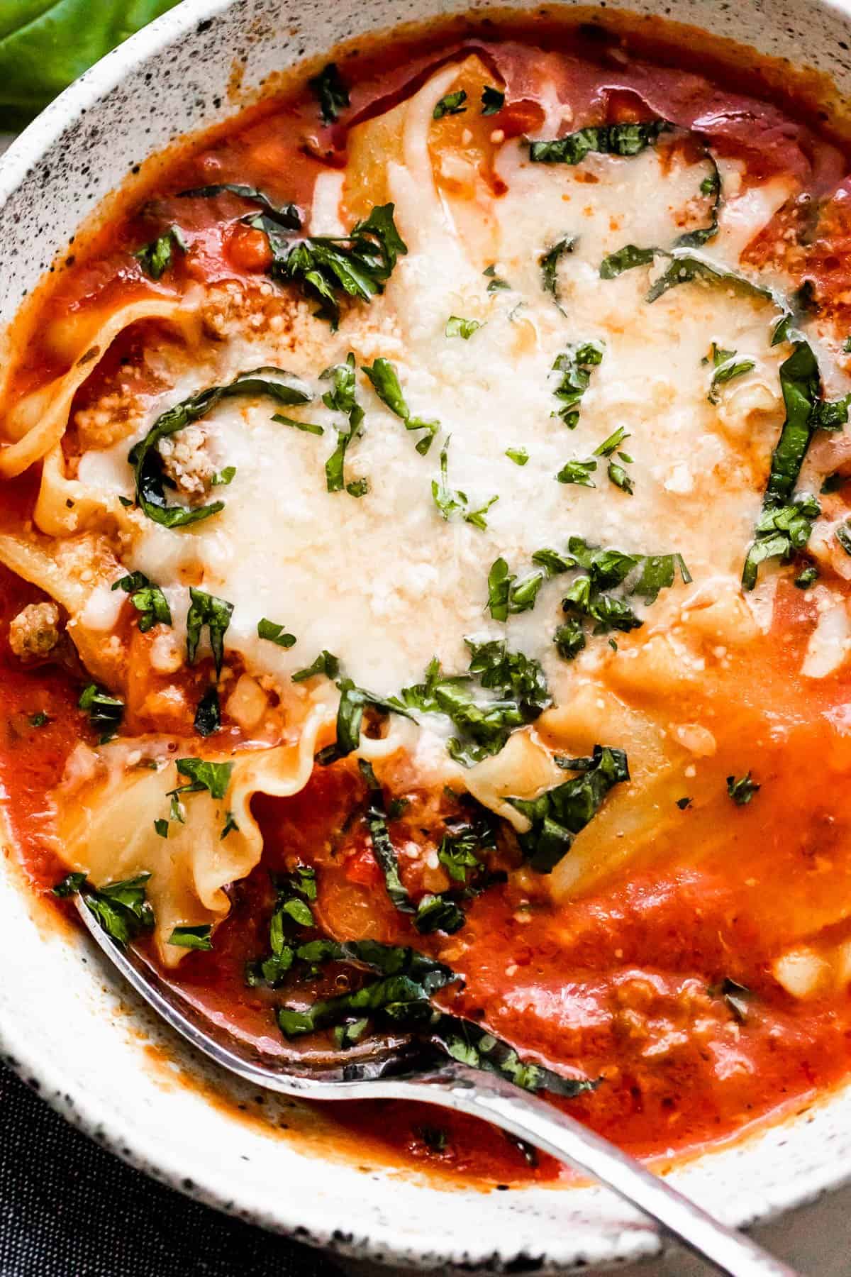 close up of a bowl with lasagna soup garnished with cheeses and basil