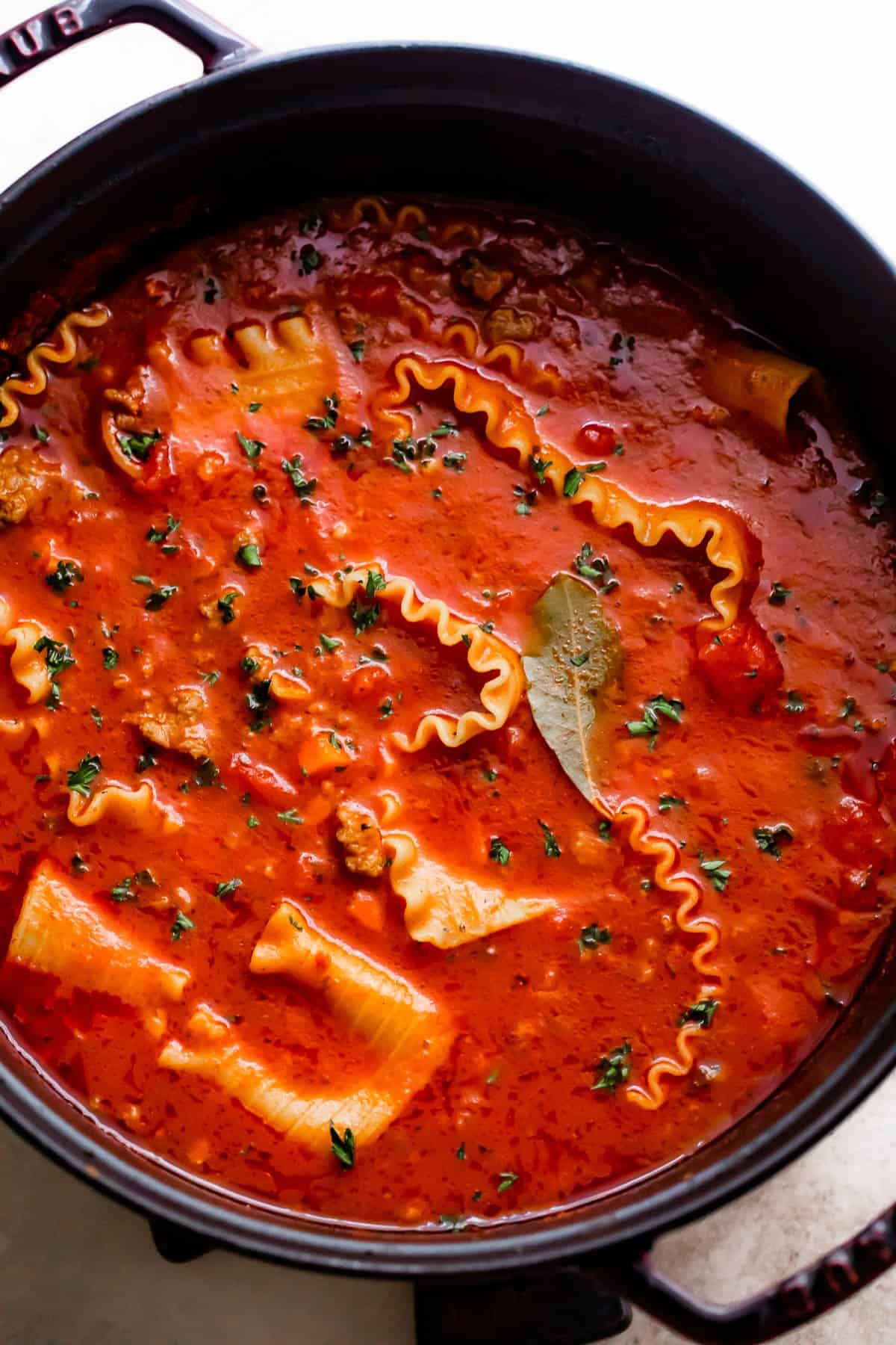 overhead shot of a dark dutch oven filled with lasagna noodles in tomato broth