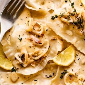 close up shot of lobster ravioli arranged on a plate and garnished with cream sauce, lemon slices, and thyme.