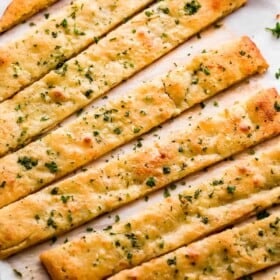 overhead shot of an oval shaped baked keto bread cut into long breadsticks, and served with marinara sauce on the side.