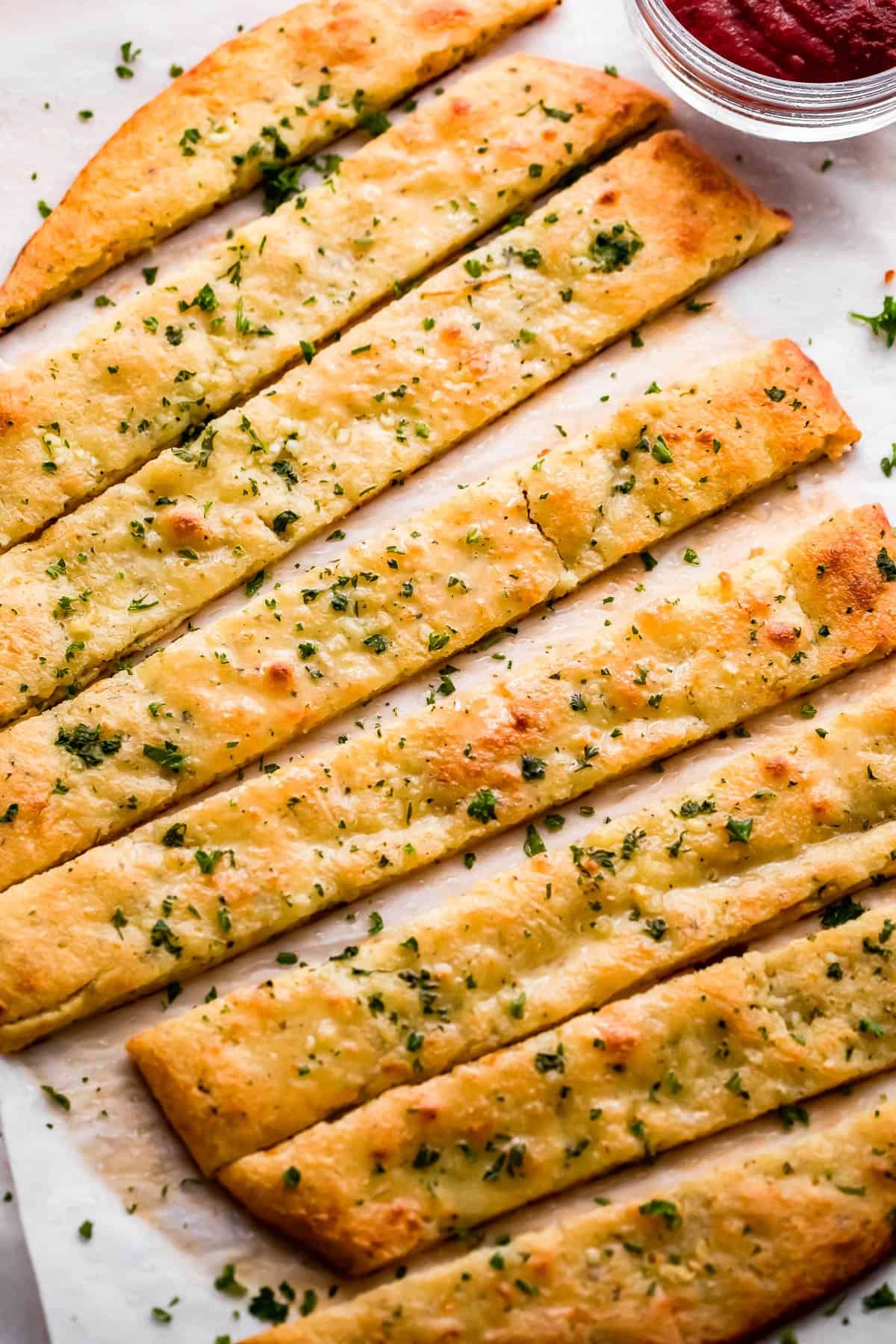 overhead shot of an oval shaped baked keto bread cut into long breadsticks, and served with marinara sauce on the side.