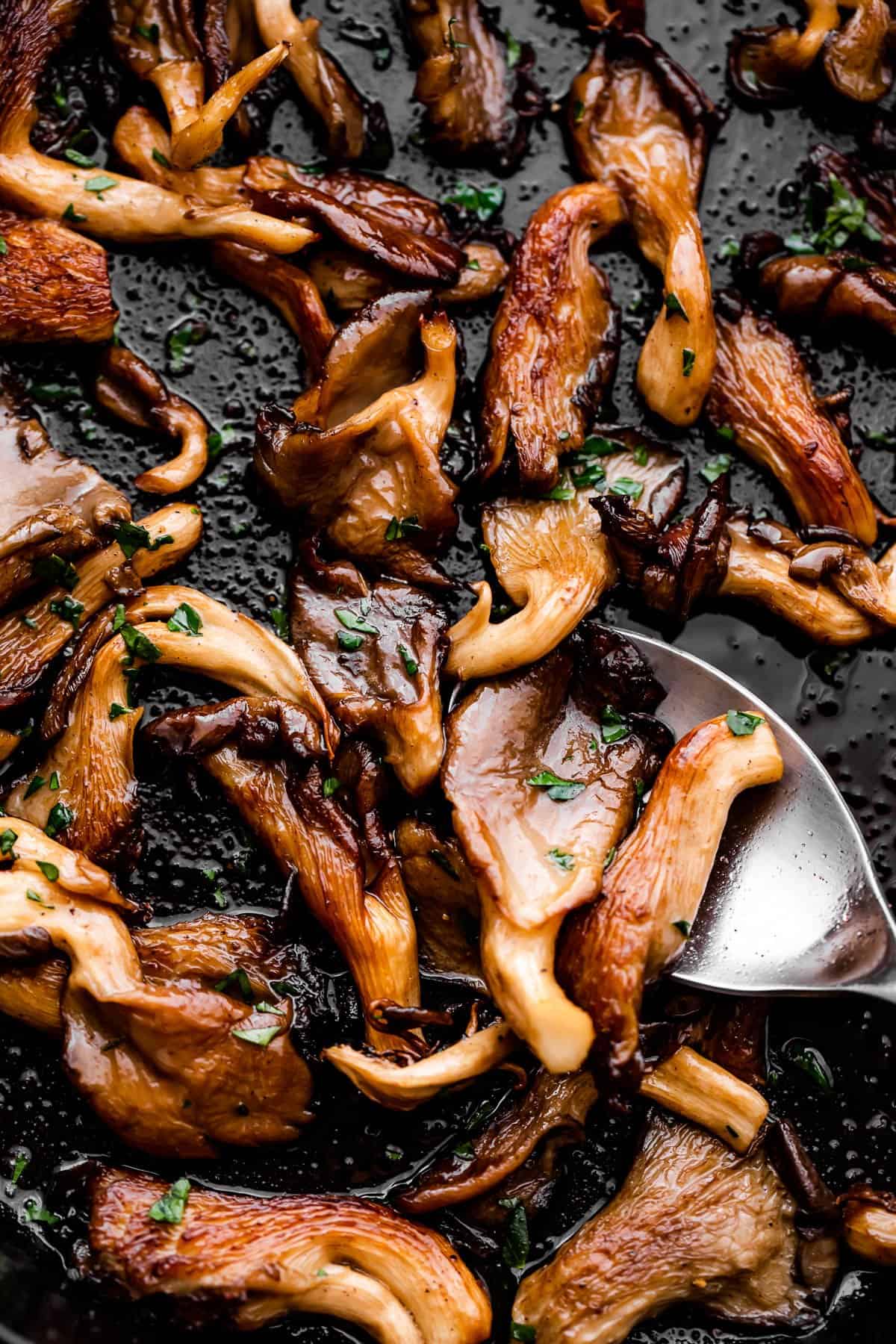 up close shot of cooked oyster mushrooms with a spoon mixing through them.