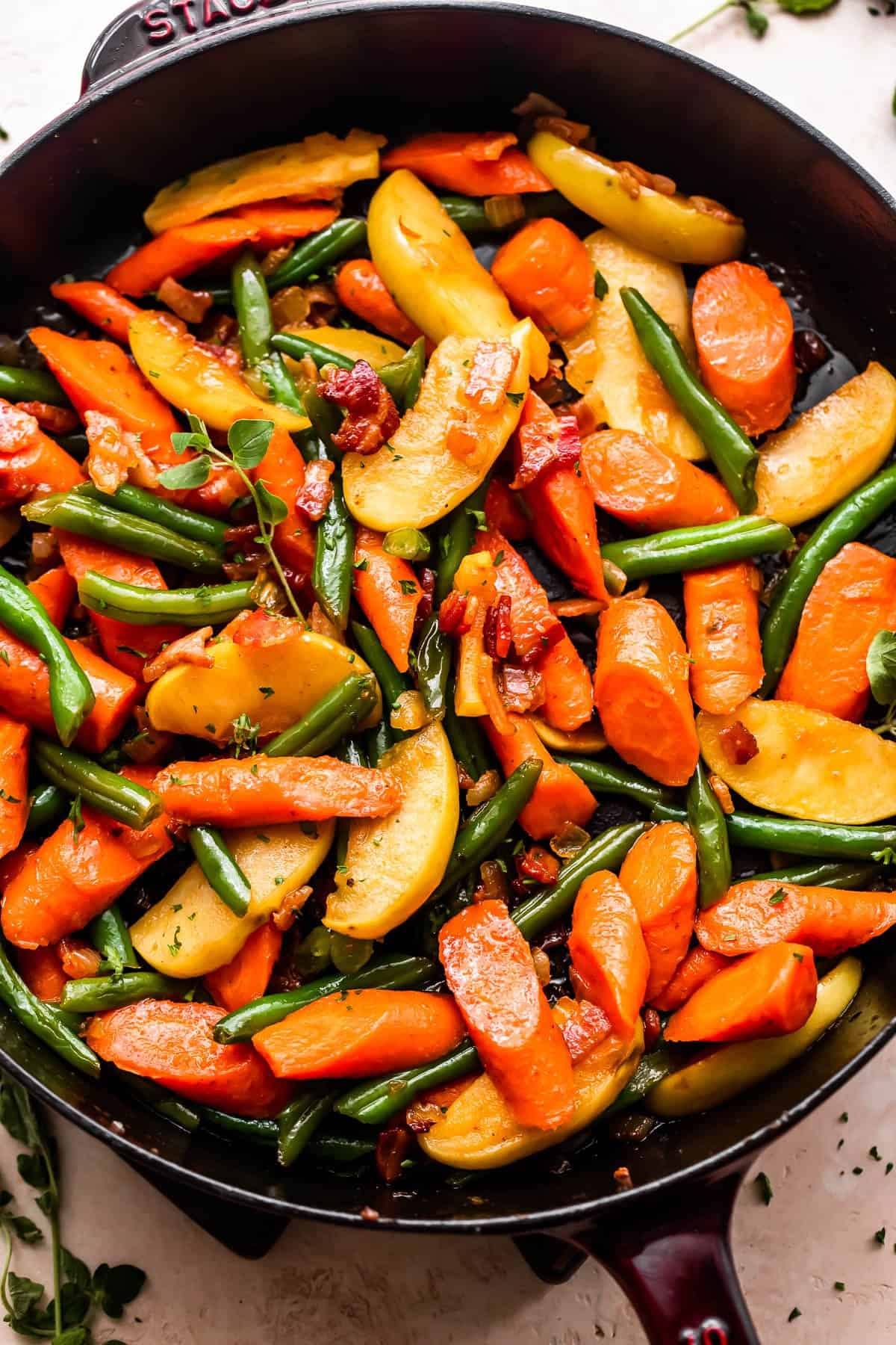 overhead shot of cooked green beans, carrots, and apples, topped with diced bacon.