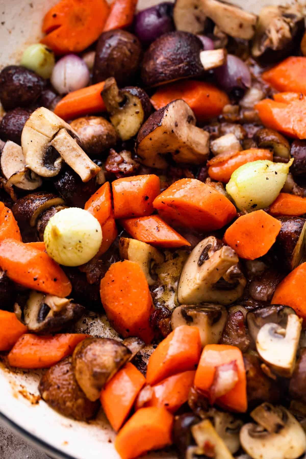 photo of a braiser filled with chopped mushrooms, carrots, and pearl onions.