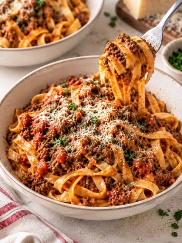Bolognese served over tagliatelle with Parmesan and parsley, with a fork twirling a bite of pasta.