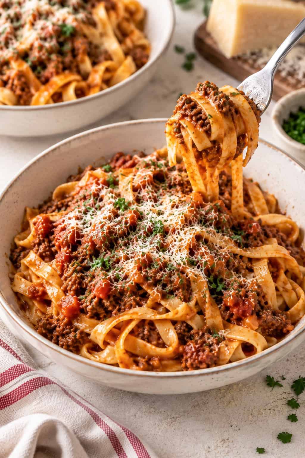 This easy Bolognese sauce recipe is made with ground beef, tomatoes, garlic, and fresh herbs, then simmered until rich and thick. Ready in about an hour! Bolognese served over tagliatelle with Parmesan and parsley, with a fork twirling a bite of pasta.