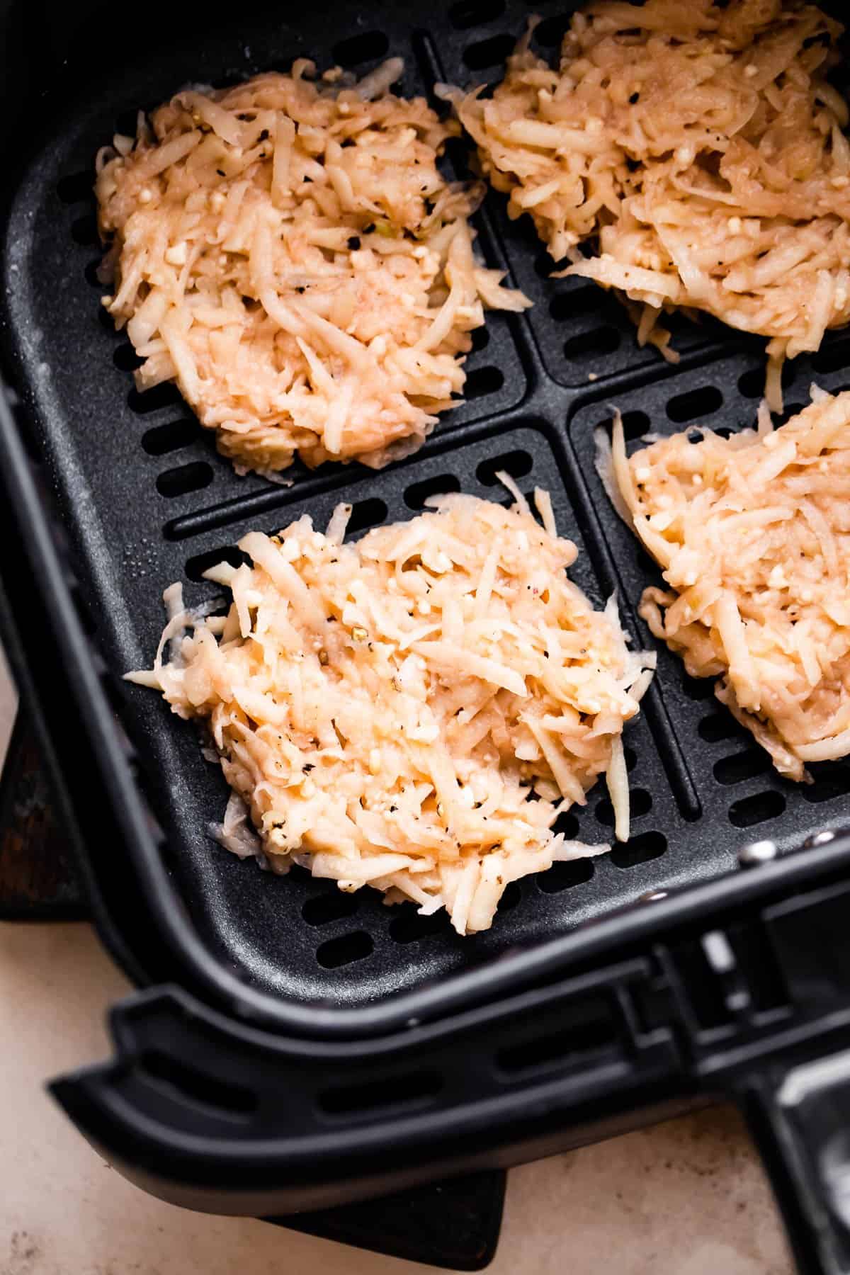 four uncooked latkes arranged inside a black air fryer basket.