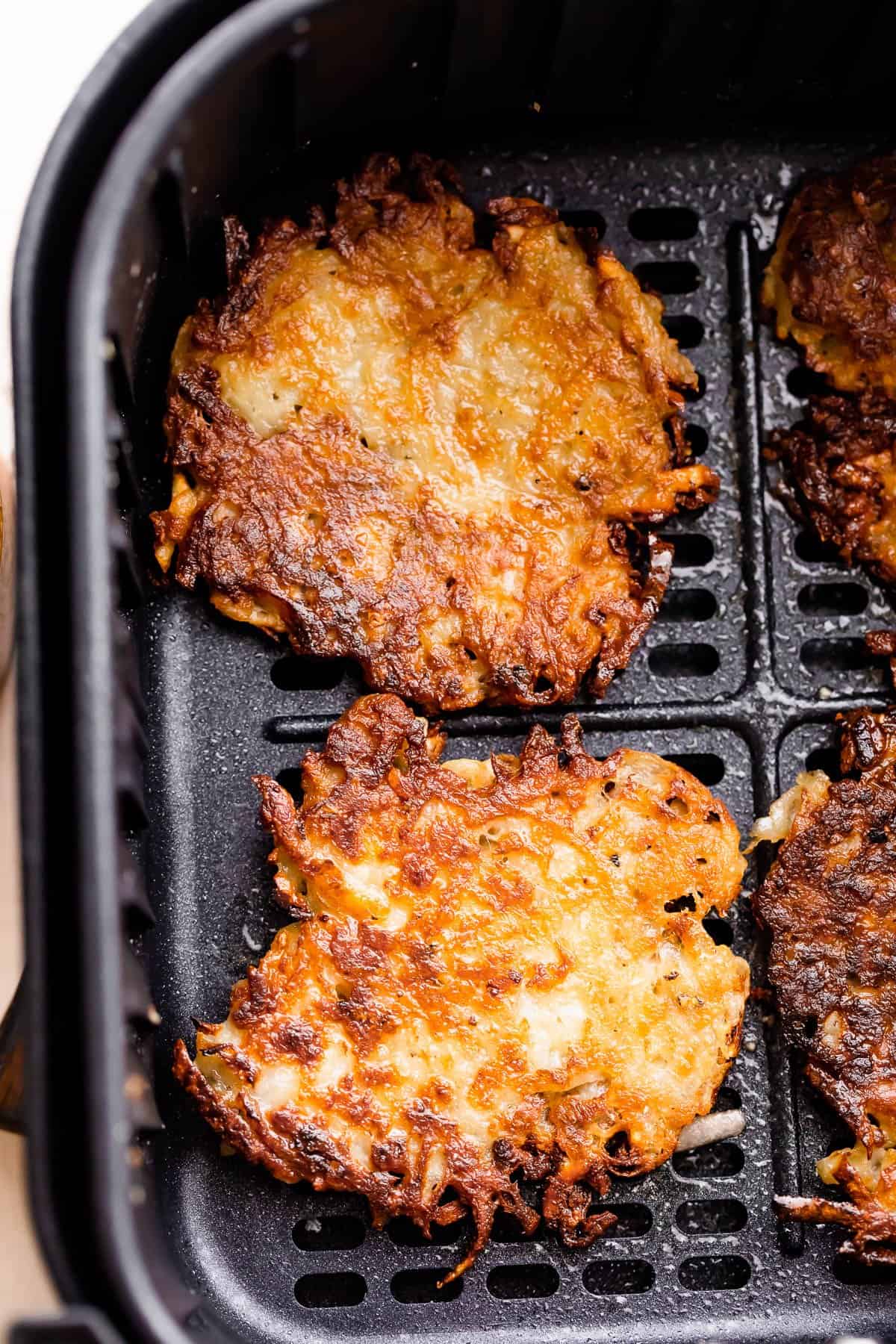 two cooked latkes inside a black air fryer basket.