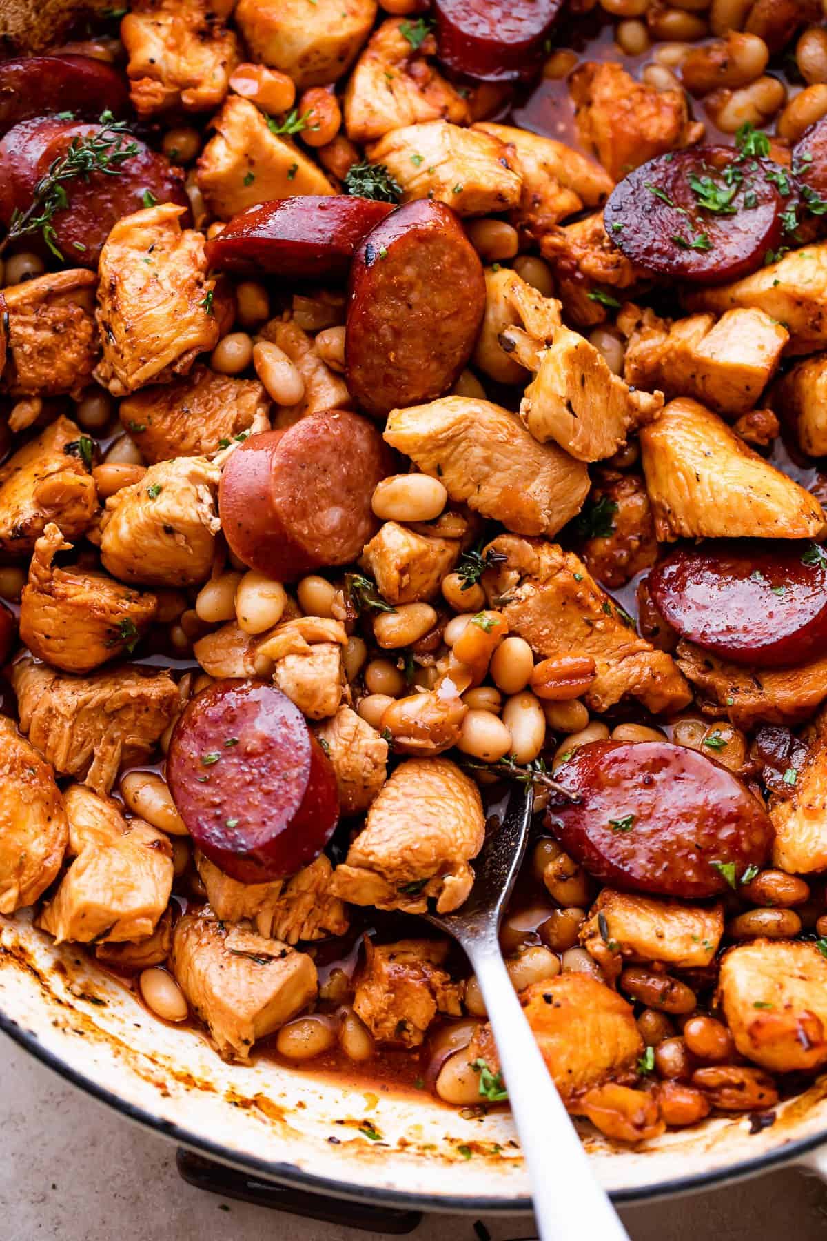 Spoon stirring through a cassoulet prepared with chicken pieces sausage.