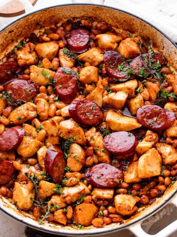 chicken pieces, beans, and smoke sausage slices in a white braiser.