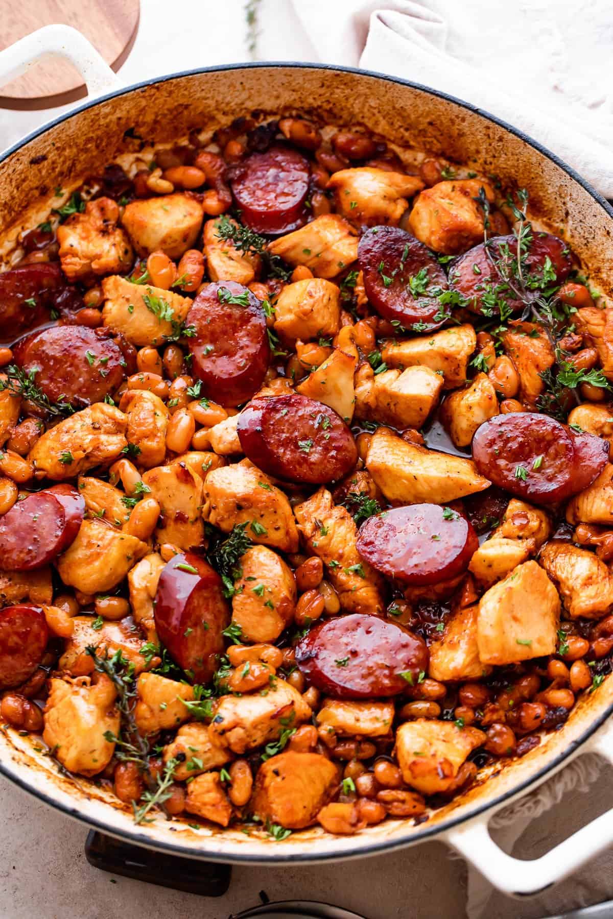 Chicken pieces, beans, and smoke sausage slices in a white braiser.