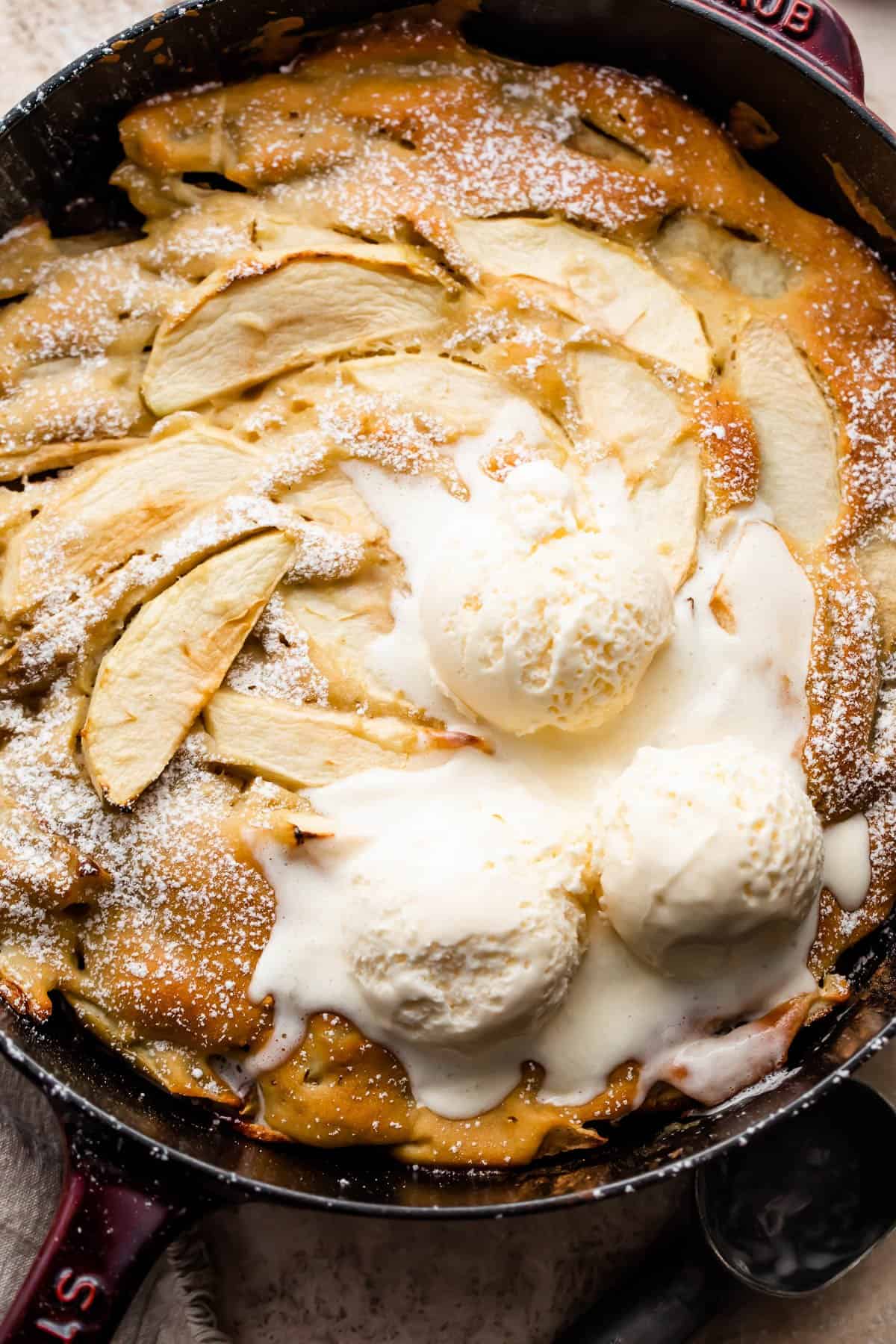 overhead shot of apple cobbler in a skillet and topped with three scoops of vanilla ice cream.