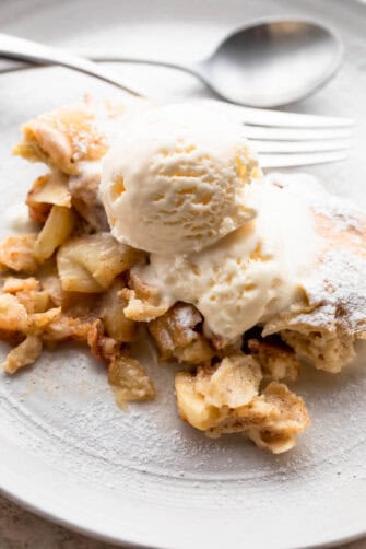 healthy apple cobbler served on a white plate, topped with a scoop of vanilla ice cream, and a spoon and fork set near the dessert.