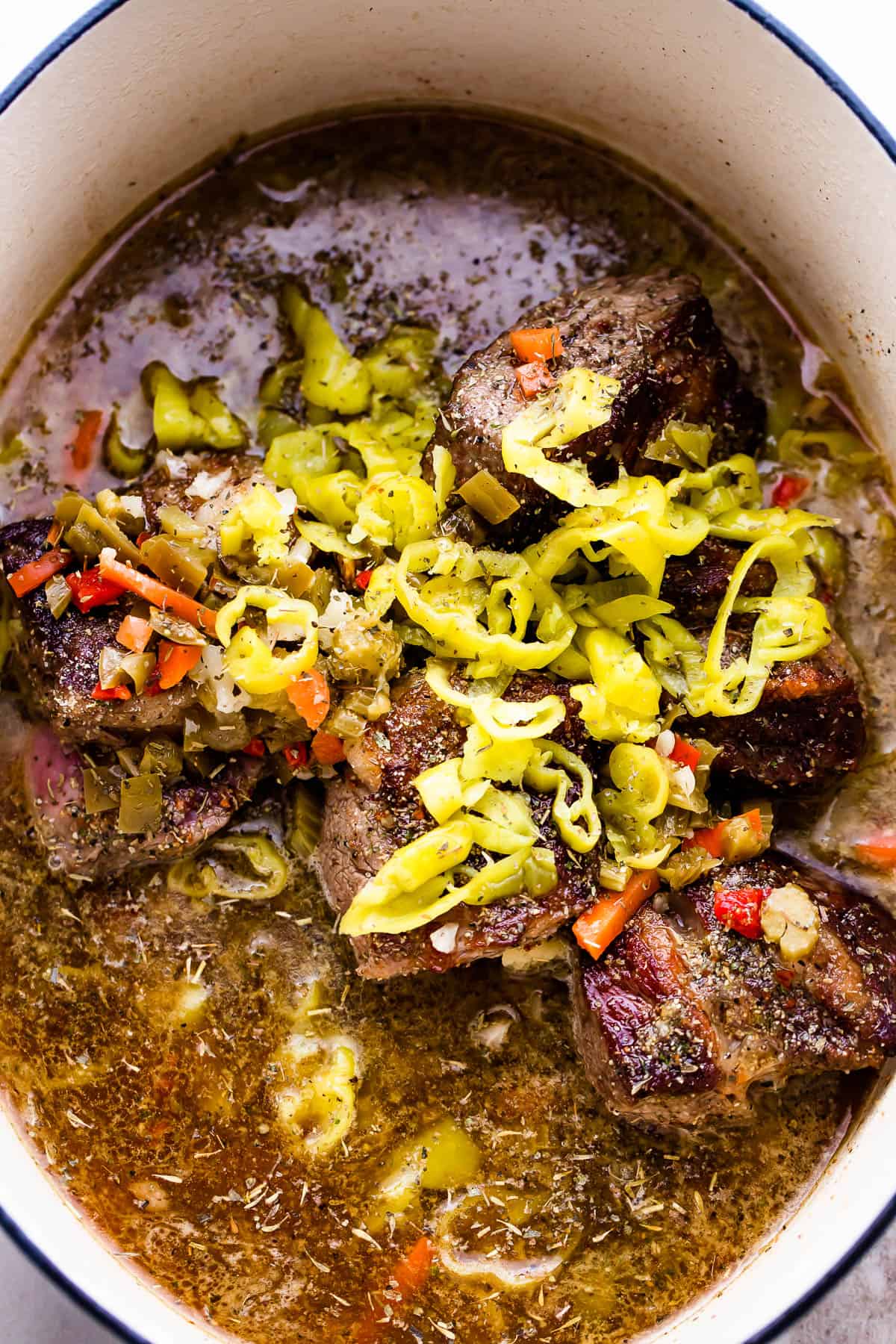 overhead shot of slow cooker insert filled with liquid, beef chuck roast, pepperoncini, and giardiniera
