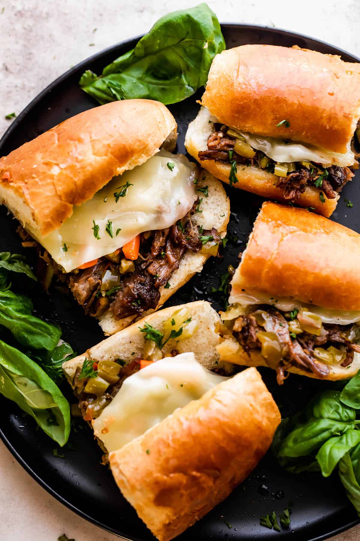 Four Slow Cooker Italian Beef Sandwiches arranged on a black plate.