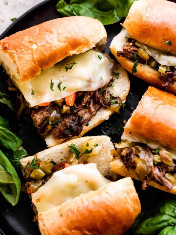 Four Slow Cooker Italian Beef Sandwiches arranged on a black plate.