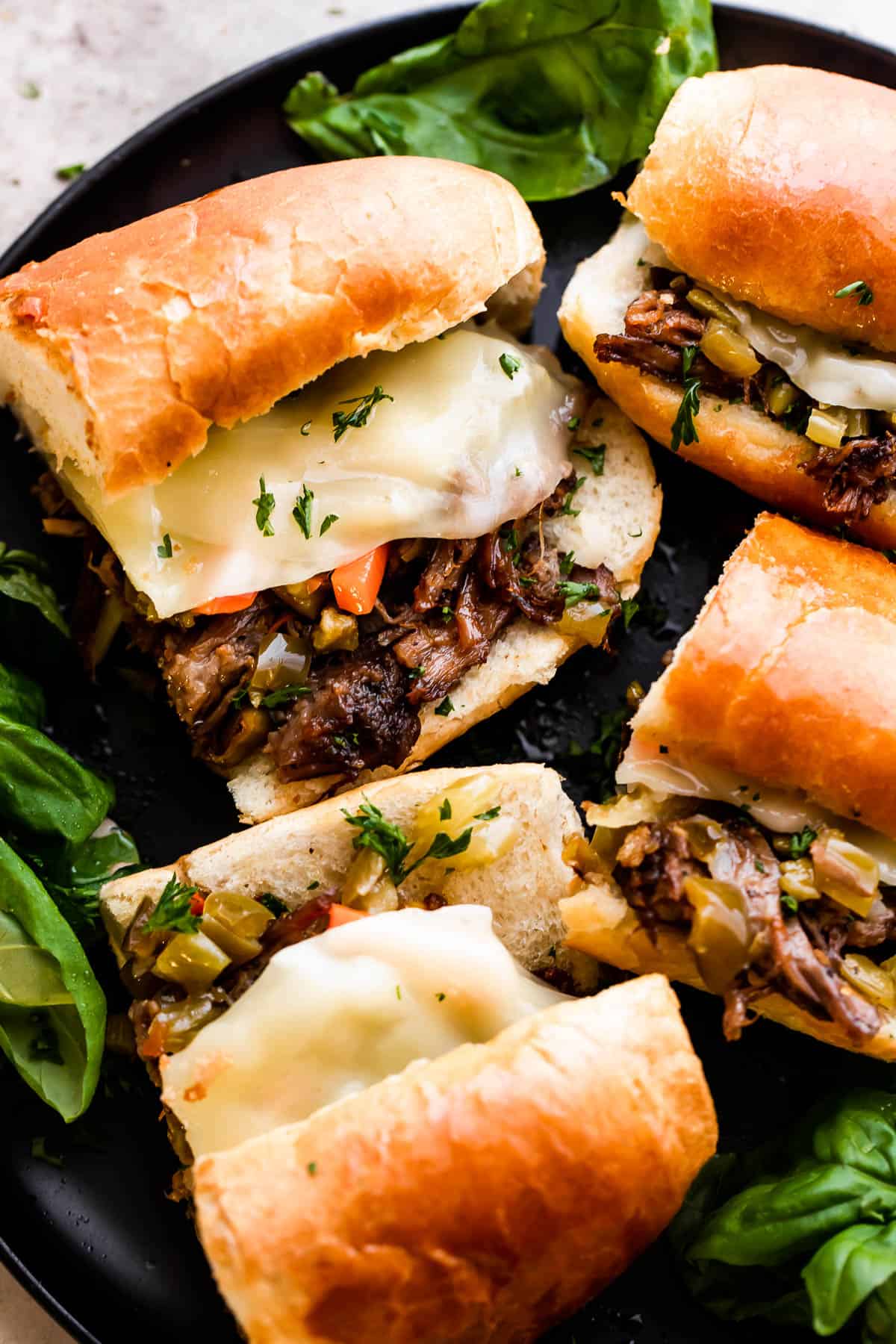 Four Slow Cooker Italian Beef Sandwiches arranged on a black plate.