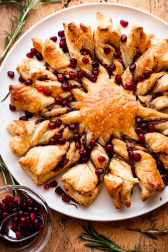 puff pastry dough shaped into a star with sixteen rays and stuffed with pesto and garnished with pomegranate arils.