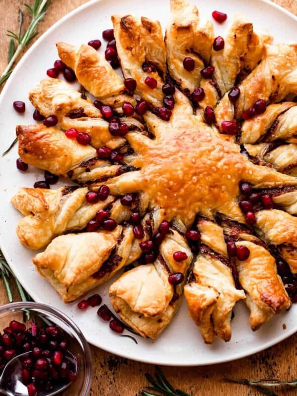 puff pastry dough shaped into a star with sixteen rays and stuffed with pesto and garnished with pomegranate arils.