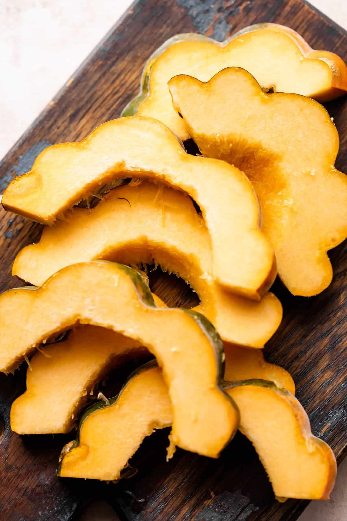 raw acorn squash cut into half-moon slices and set on a wooden board.