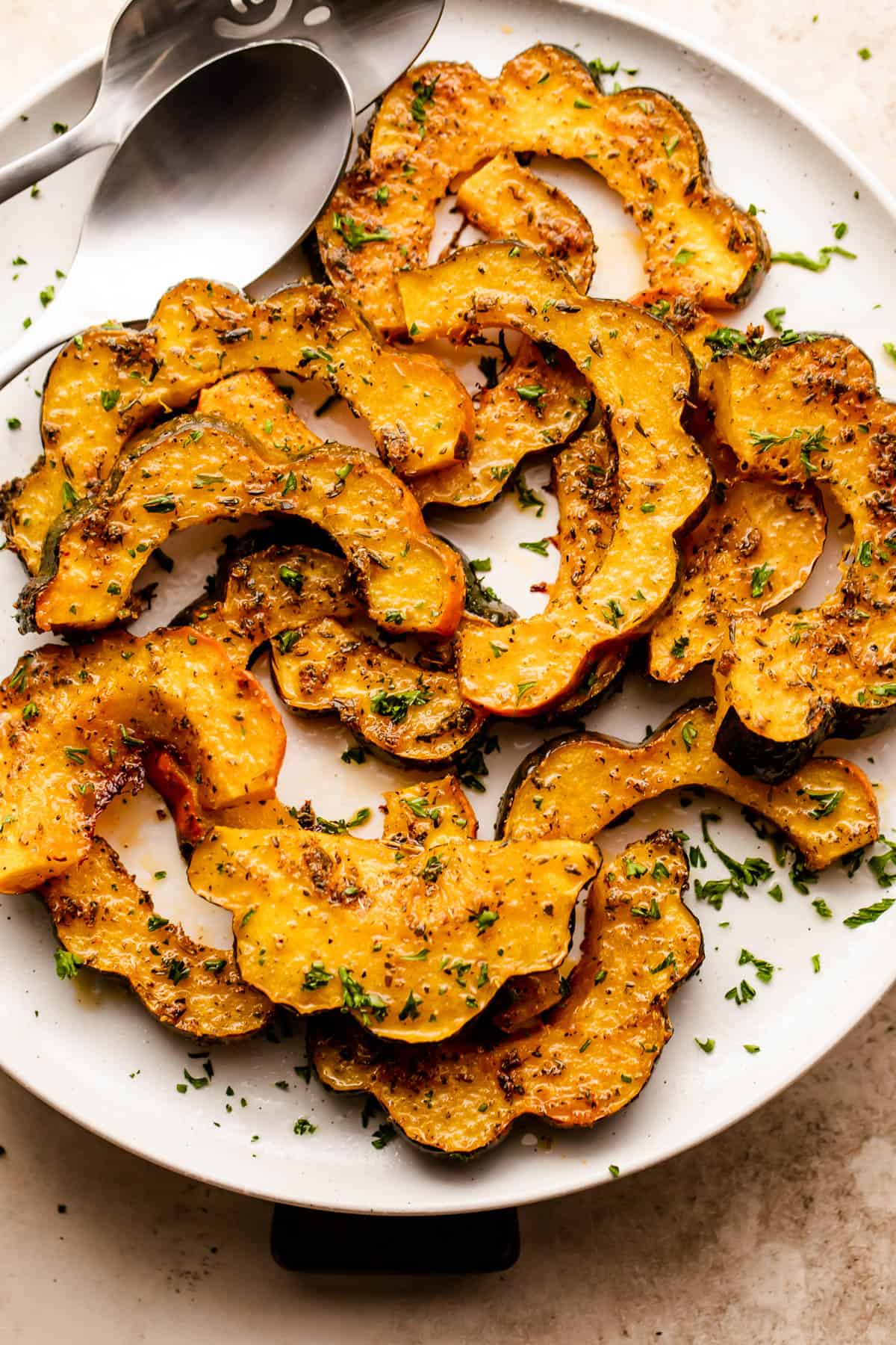 roasted acorn squash cut into half-moon slices, arranged on a white plate and seasoned with oil and herbs.