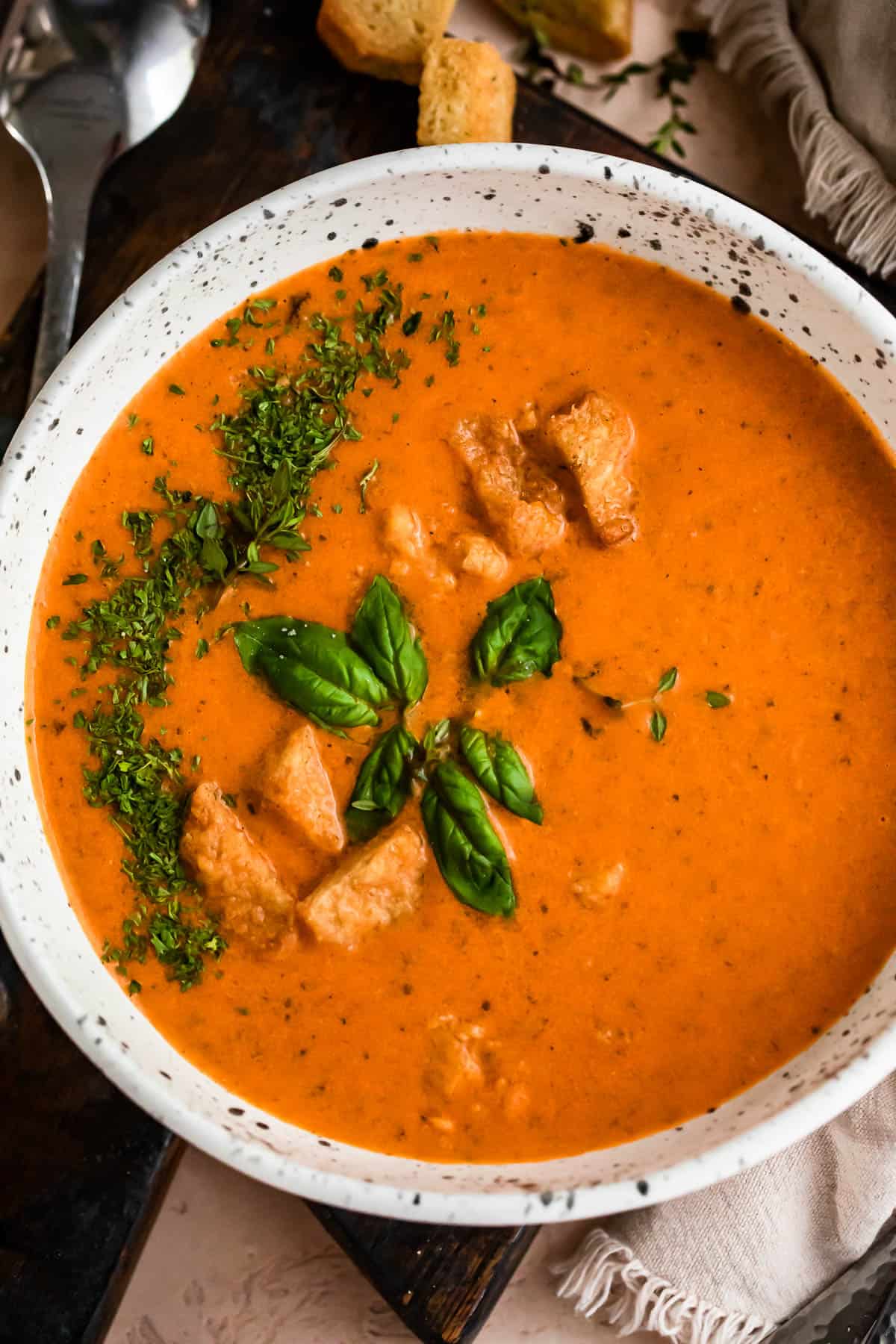 overhead shot of Roasted Tomato Basil Soup in a bowl and garnished with basil and croutons.