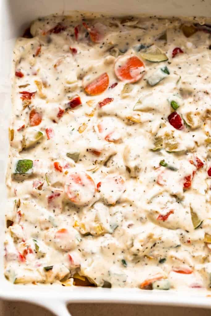 a mixture of creamy cheeses and vegetables arranged in a baking dish.