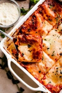 overhead shot of a square baking dish with vegetable lasagna cut in squares and one square being lifted up with a spoon.